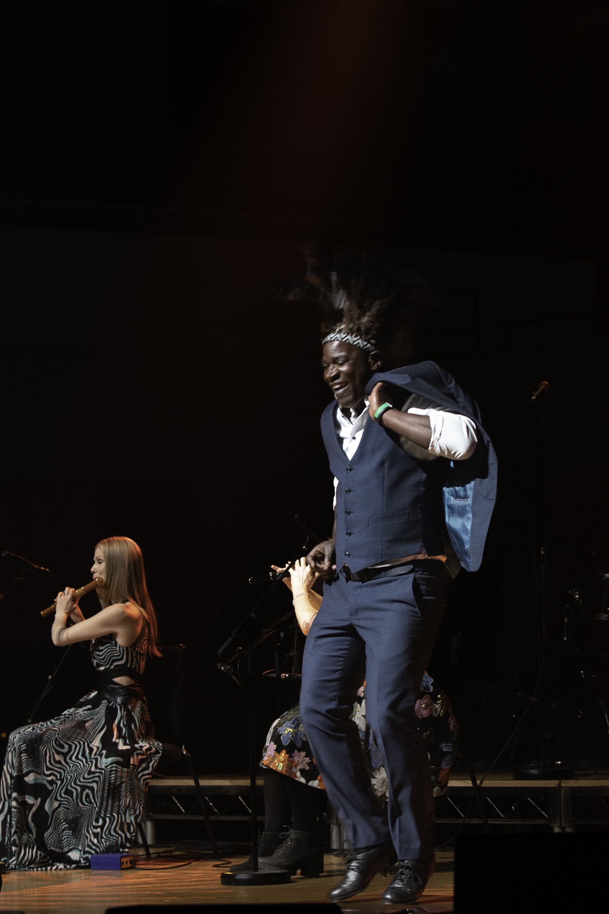 Tura Arutura dancing mid-air on a concert stage beside traditional Irish musicians