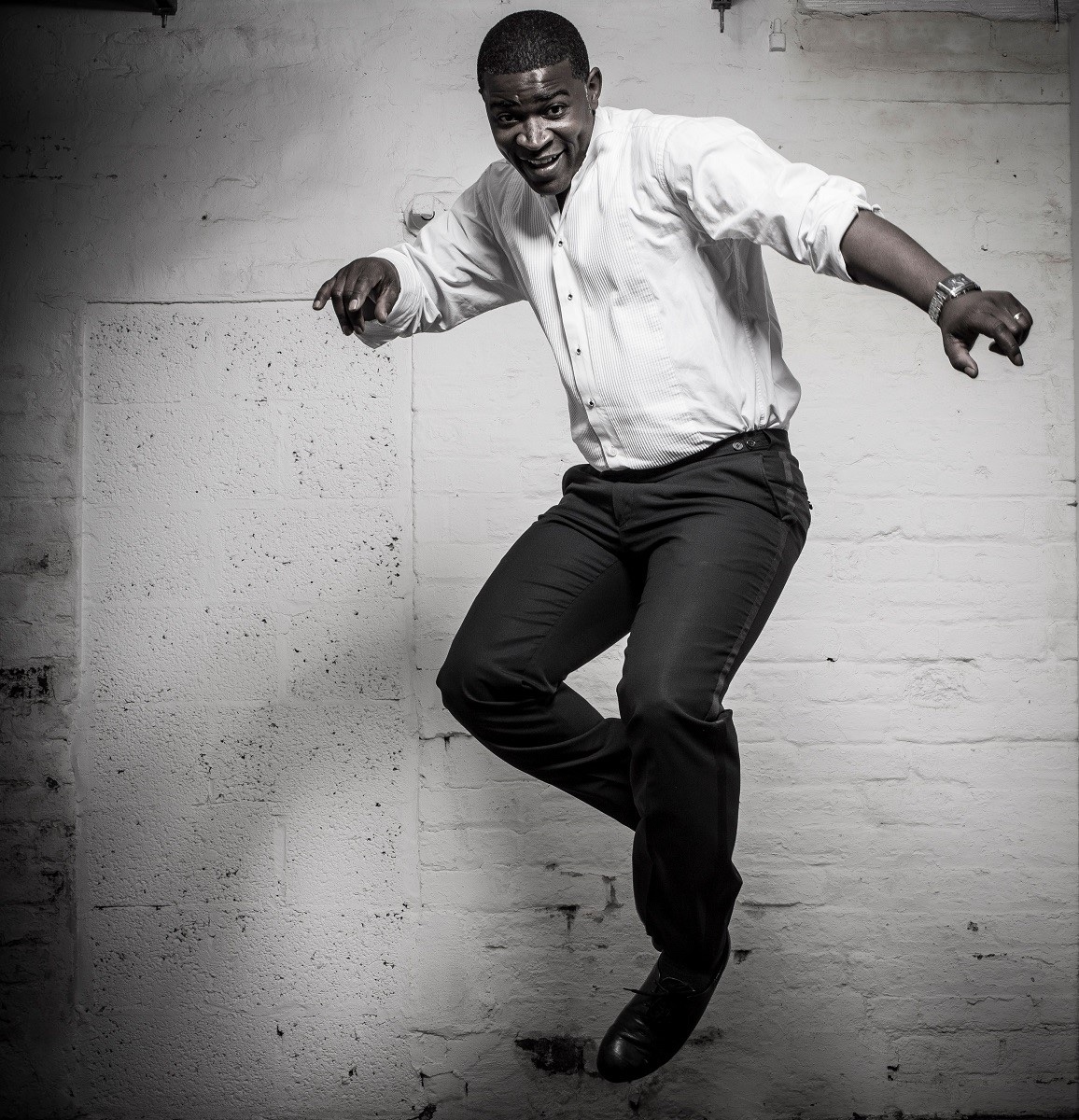 Tura Arutura mid-leap in a white shirt against a whitewashed brick wall